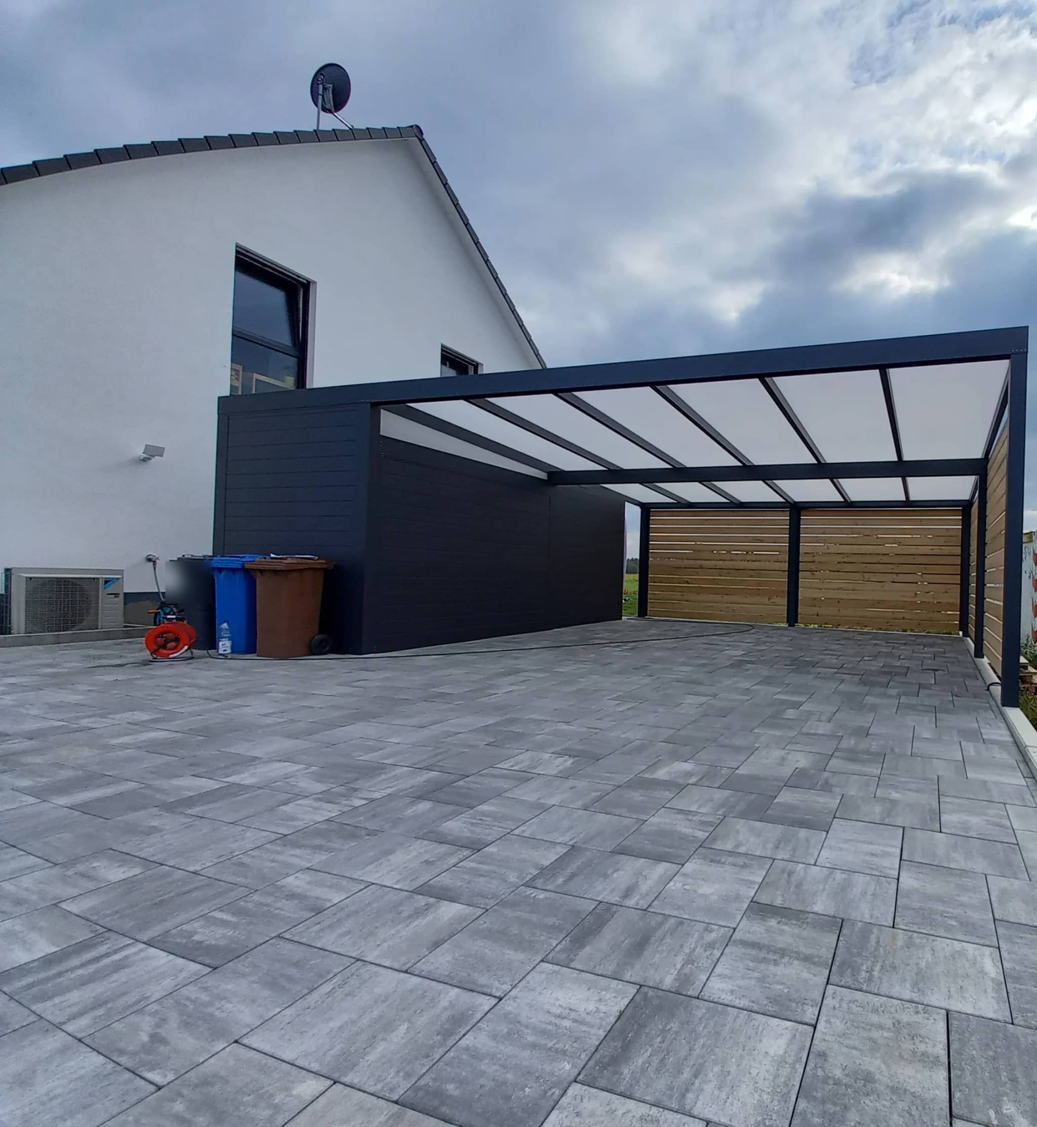 Freistehender Aluminium-Carport in Anthrazit mit Geräteschuppen über gepflasterter Zufahrt