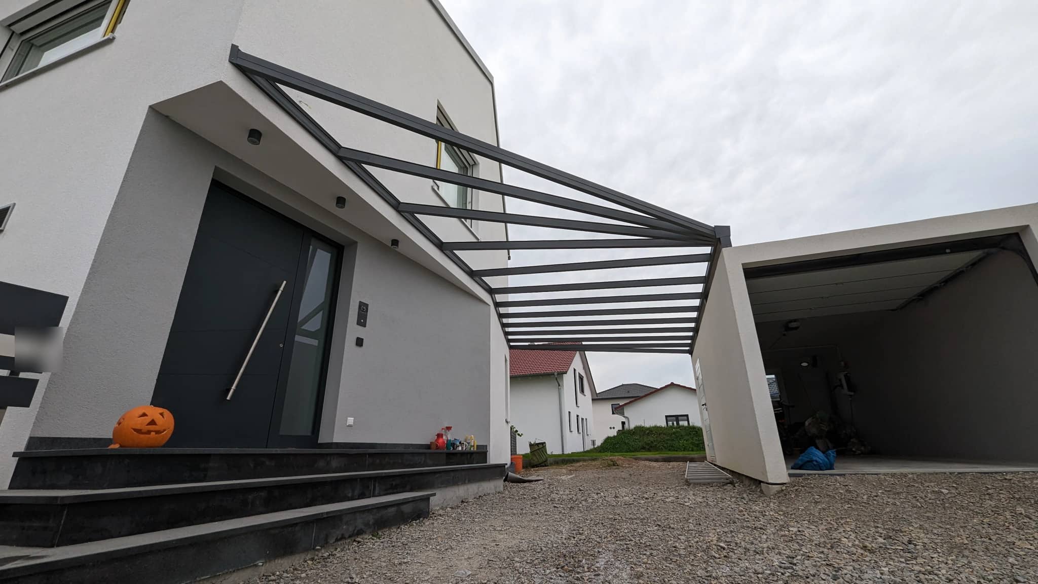Carport aus anthrazitfarbenem Aluminium mit lichtdurchlässiger Eindeckung, überdachter Zugang zwischen Hauseingang und Garage