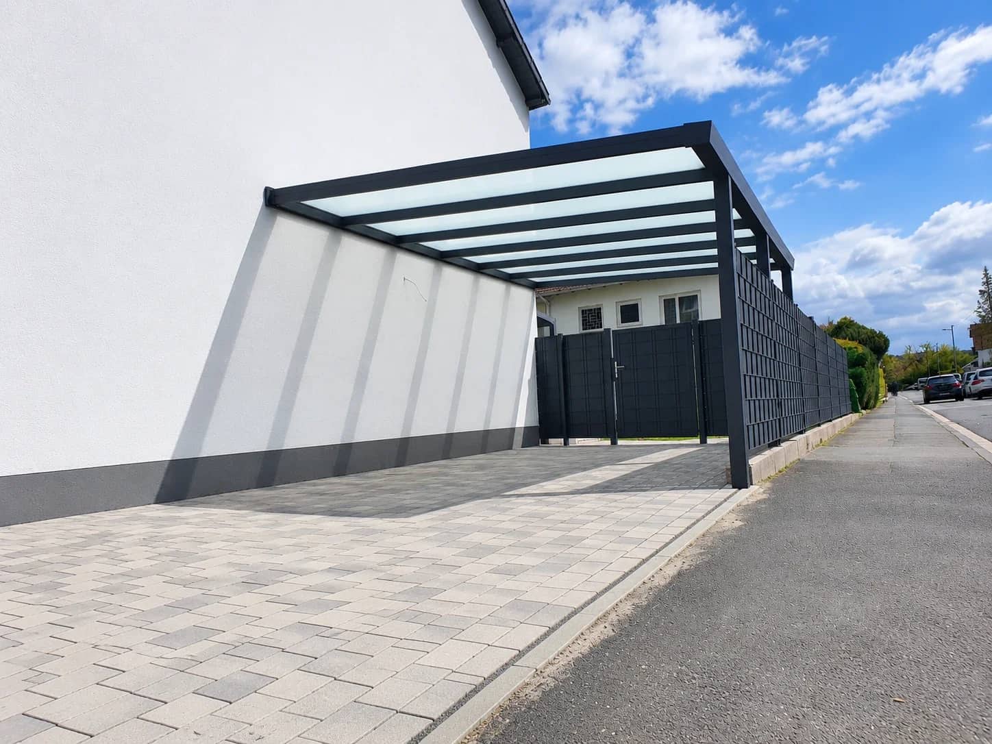 Carport aus Aluminium in Anthrazit: schlankes Pultdach mit lichtdurchlässiger Eindeckung entlang der Einfahrt