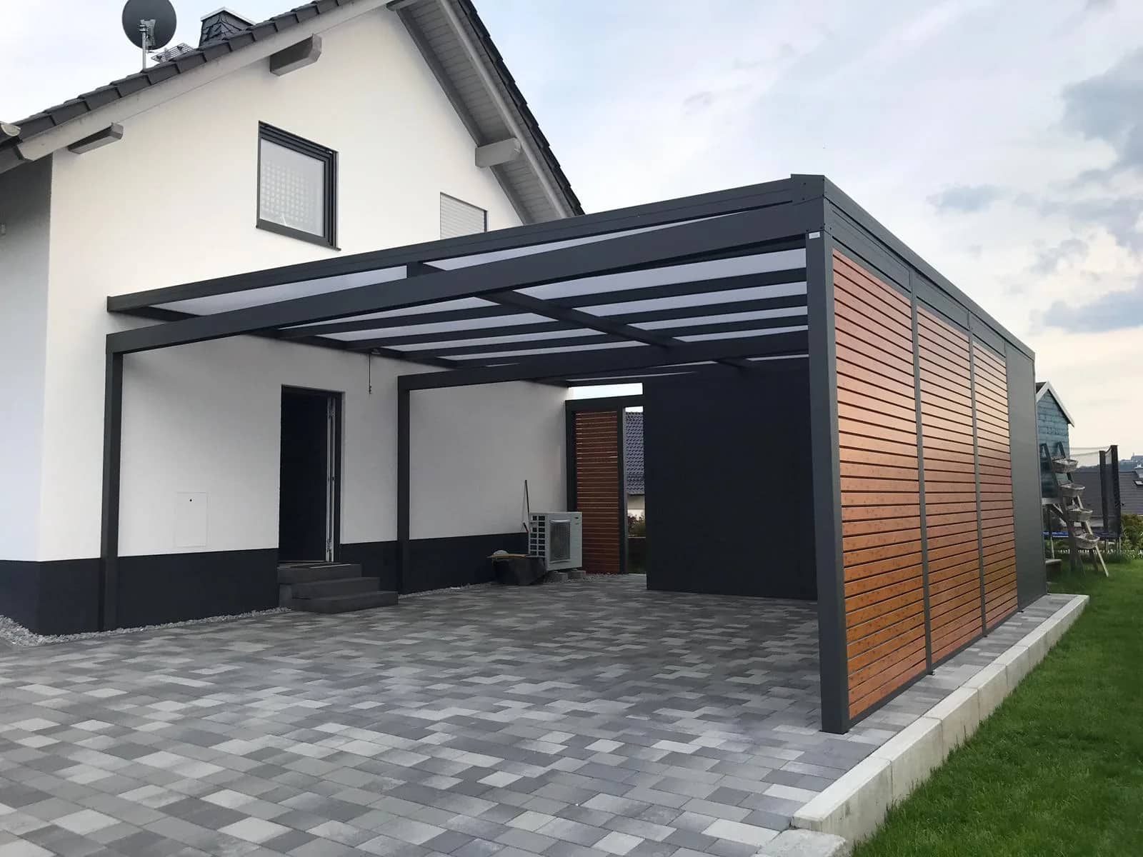 Carport aus Aluminium in Anthrazit mit lichtdurchlässiger Eindeckung und seitlicher Verkleidung in Holzoptik am Wohnhaus