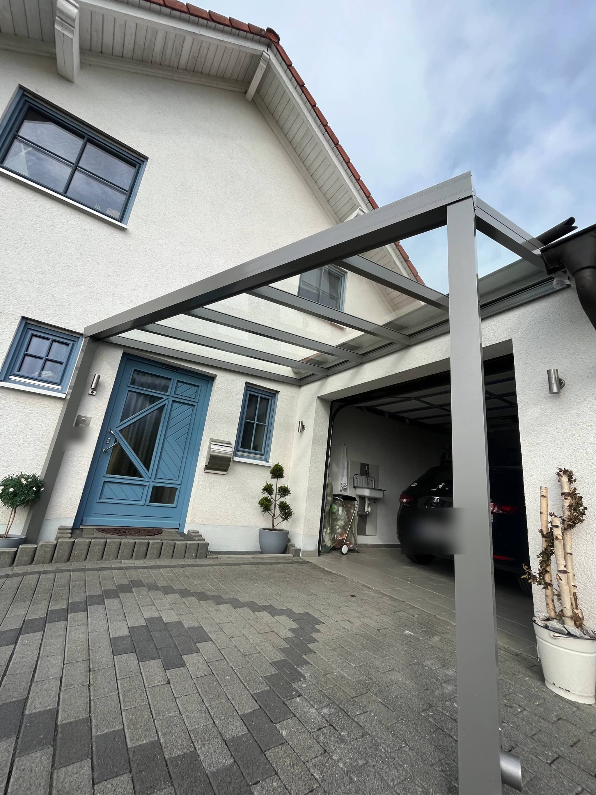 Eingangsüberdachung aus Aluminium mit lichtdurchlässigem Dach über dem Hauseingang, daneben ein überdachter Stellplatz