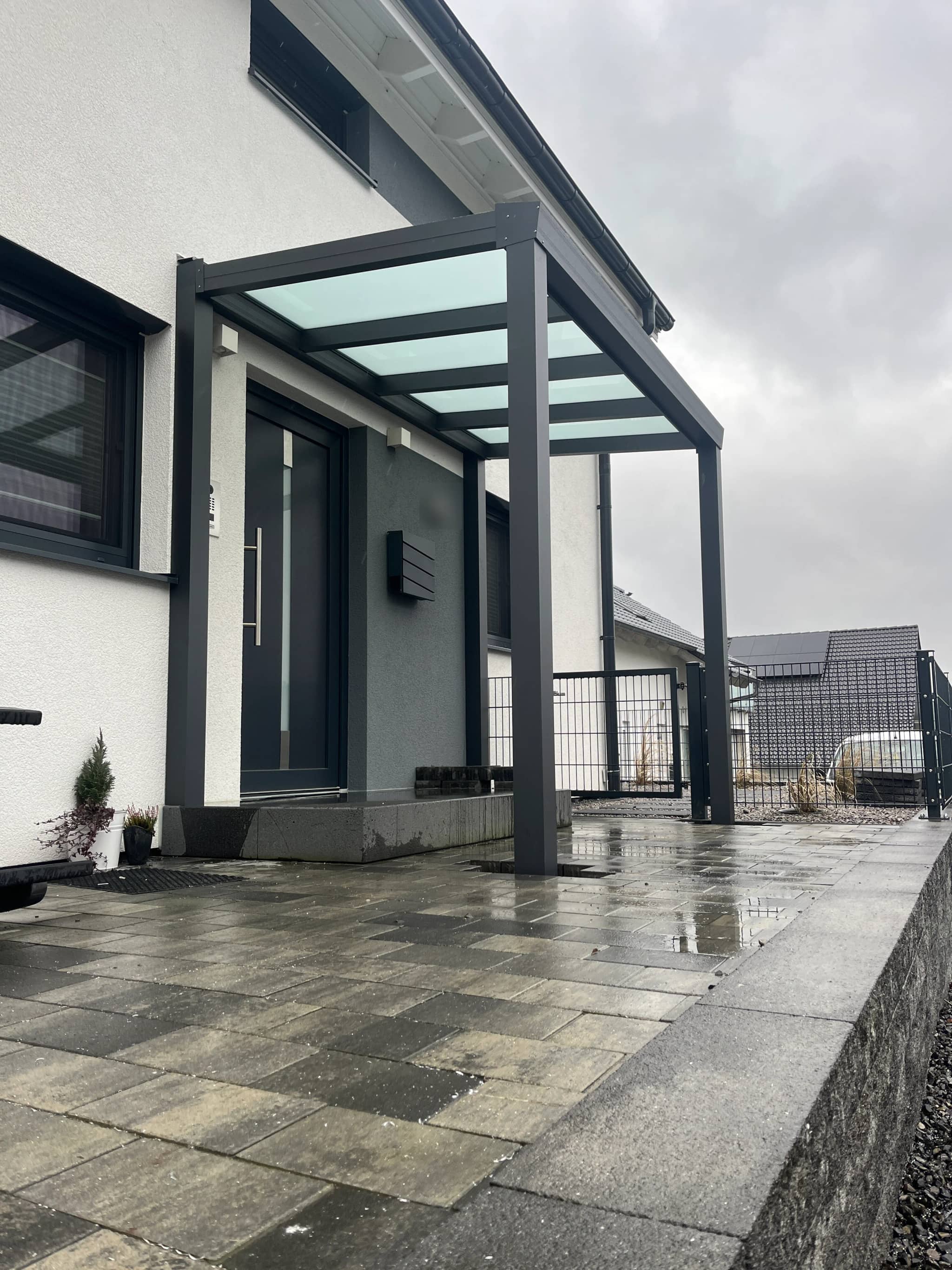 Eingangsüberdachung aus anthrazitfarbenem Aluminium mit lichtdurchlässiger Eindeckung, wettergeschützter Hauseingang an moderner Fassade