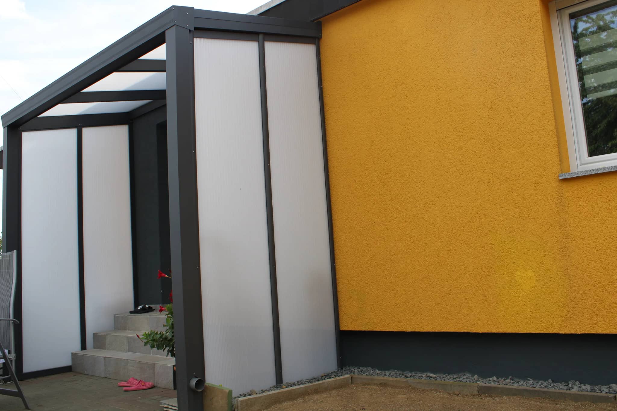 Überdachter Treppenaufgang aus Aluminium in Anthrazit mit geschlossenen, lichtdurchlässigen Seitenwänden am Seiteneingang