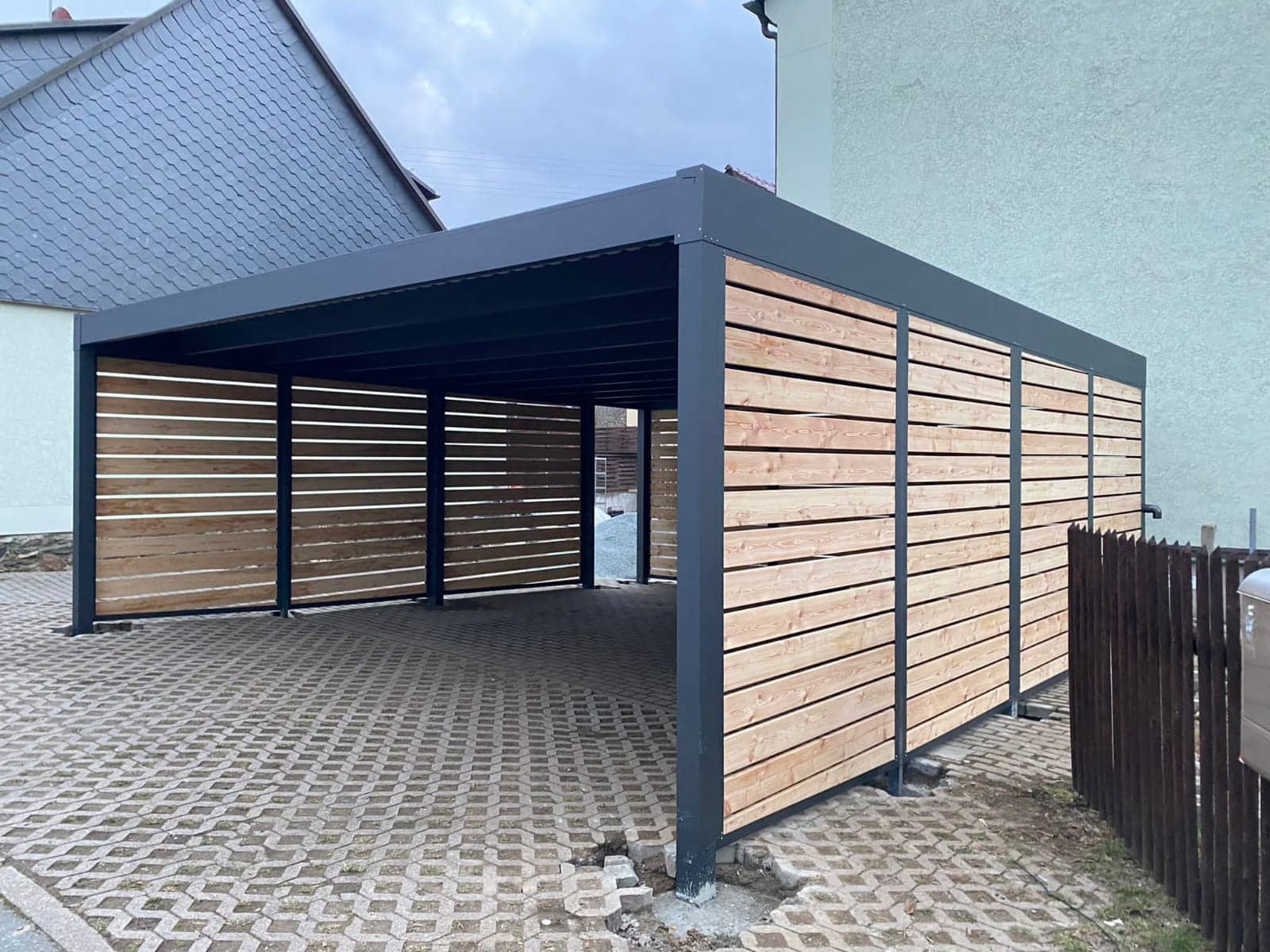 Flachdach-Carport aus Aluminium in Anthrazit mit Seitenwänden in Holzoptik über Rasengittersteinen