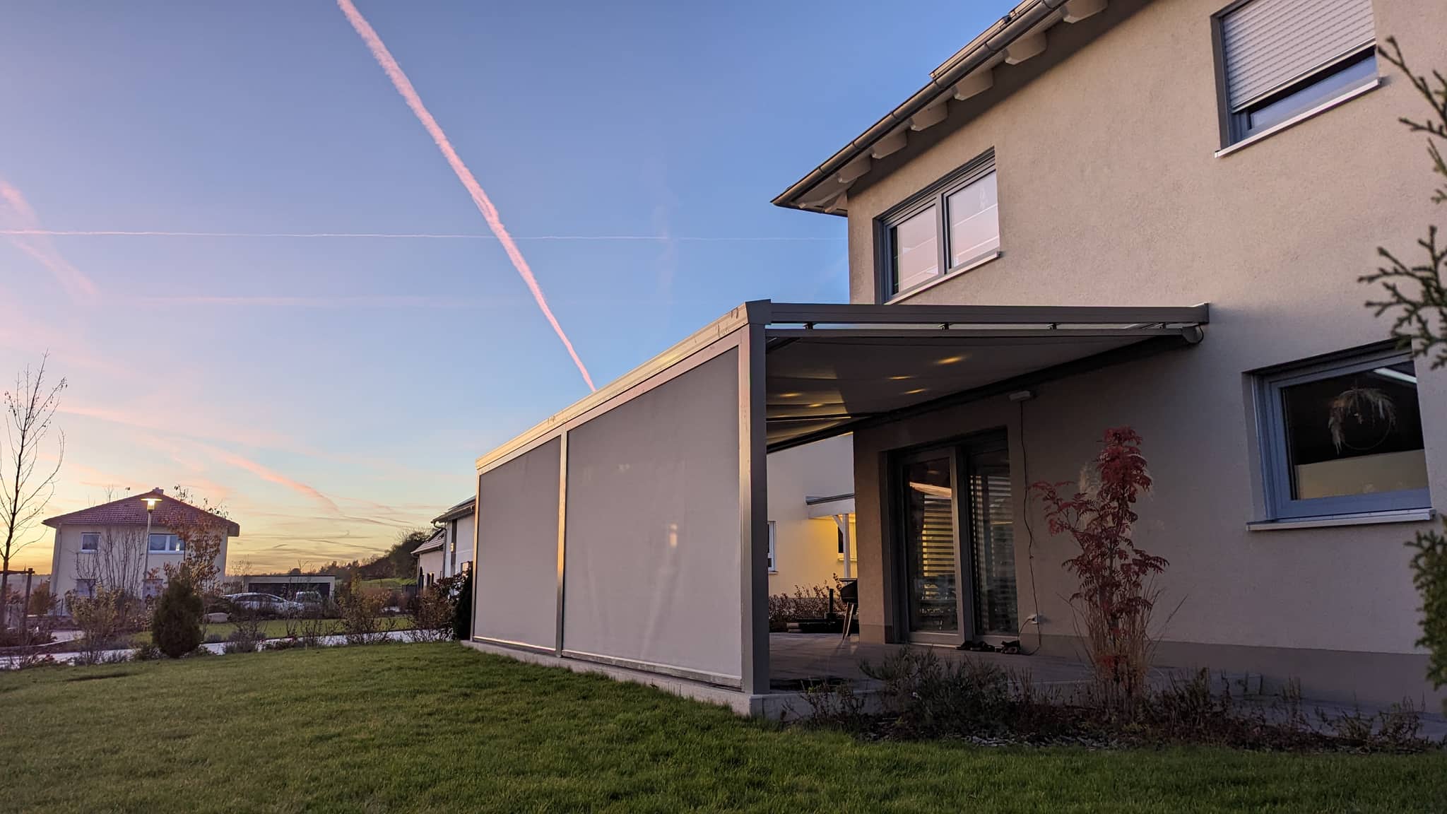Terrassenüberdachung mit heruntergelassenen Senkrechtmarkisen an einem Wohnhaus im Abendlicht
