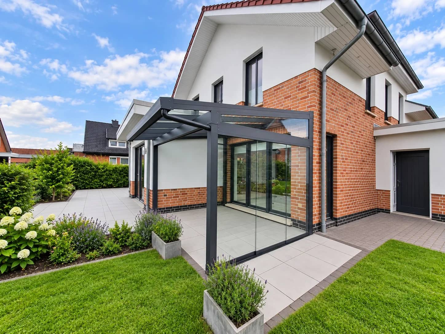 Sommergarten aus Aluminium in Anthrazit mit lichtdurchlässigem Glasdach und rahmenloser Glasfront an weißem Wohnhaus