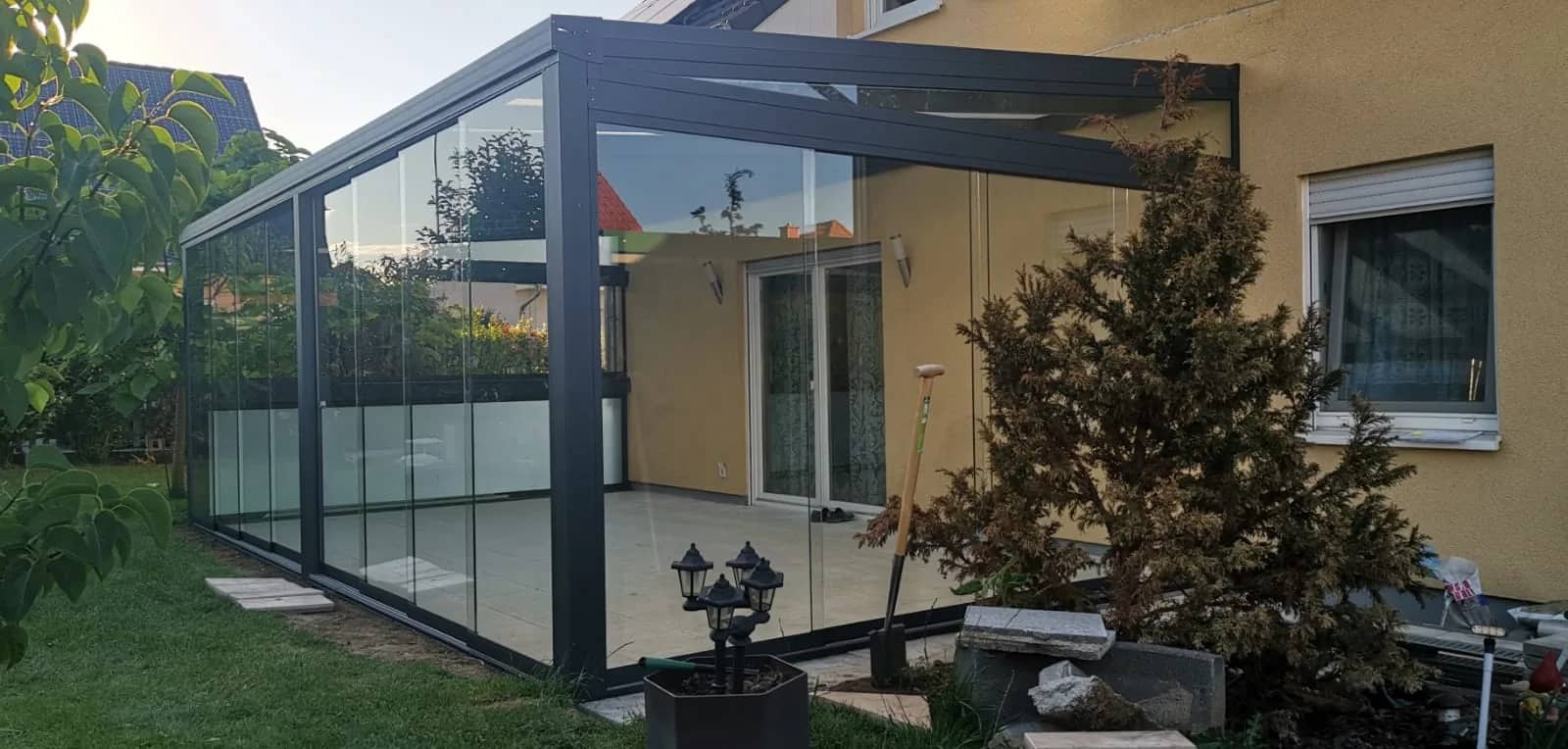 Terrassenüberdachung aus Aluminium in Anthrazit mit Glas-Schiebeanlage an einem gelben Wohnhaus