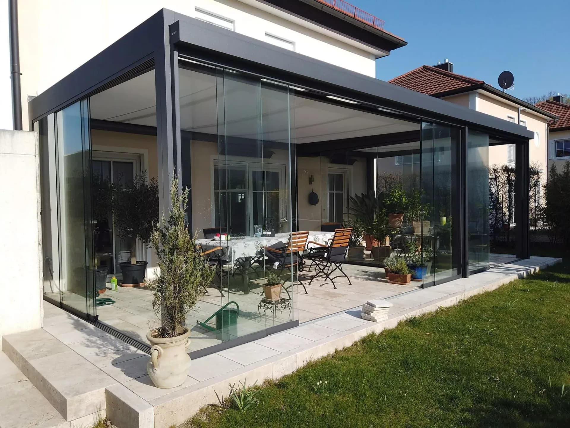 Glas-Schiebeanlage mit anthrazitfarbenem Rahmen als Windschutz an der Terrasse