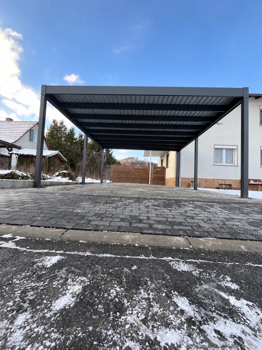 Carport freistehend mit anthrazitfarbenem Aluminiumrahmen und Flachdach, offene Stellfläche mit gepflastertem Boden im Winter