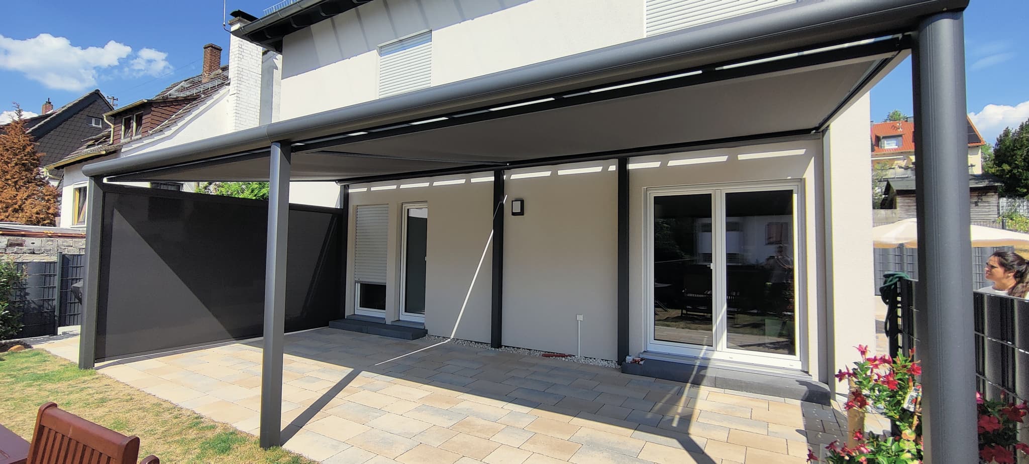 Terrassenüberdachung aus Aluminium in Anthrazit mit dunkler, geschlossener Panelwand an einer Seite über einer Plattenterrasse