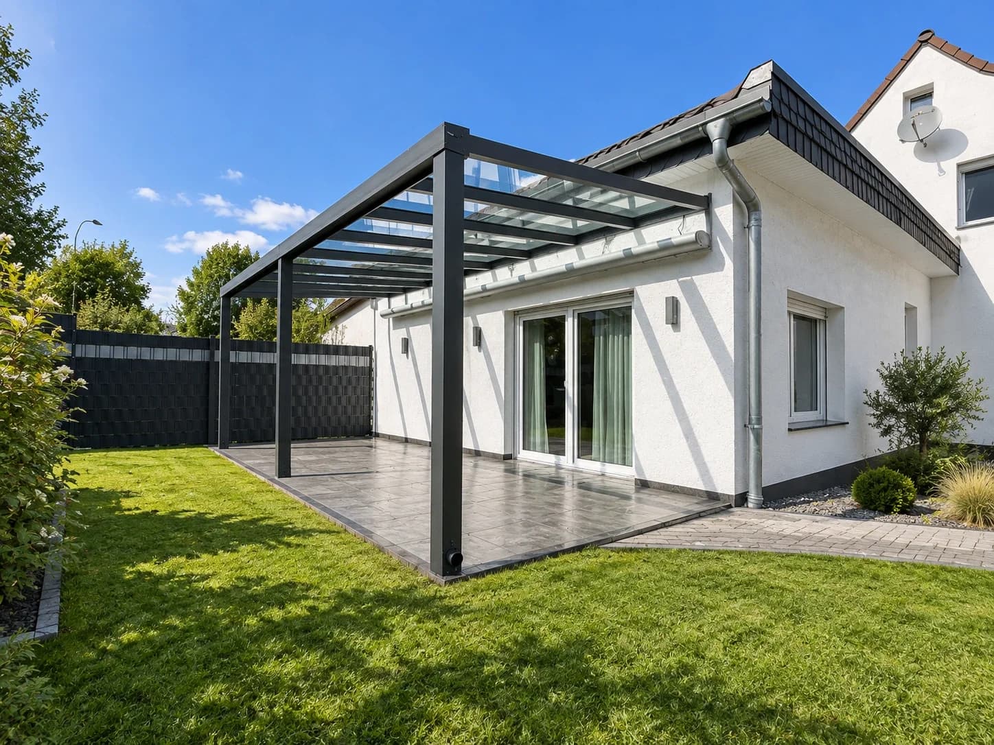 Terrassenüberdachung aus Aluminium in Anthrazit mit klarer Glaseindeckung an einem weißen Wohnhaus