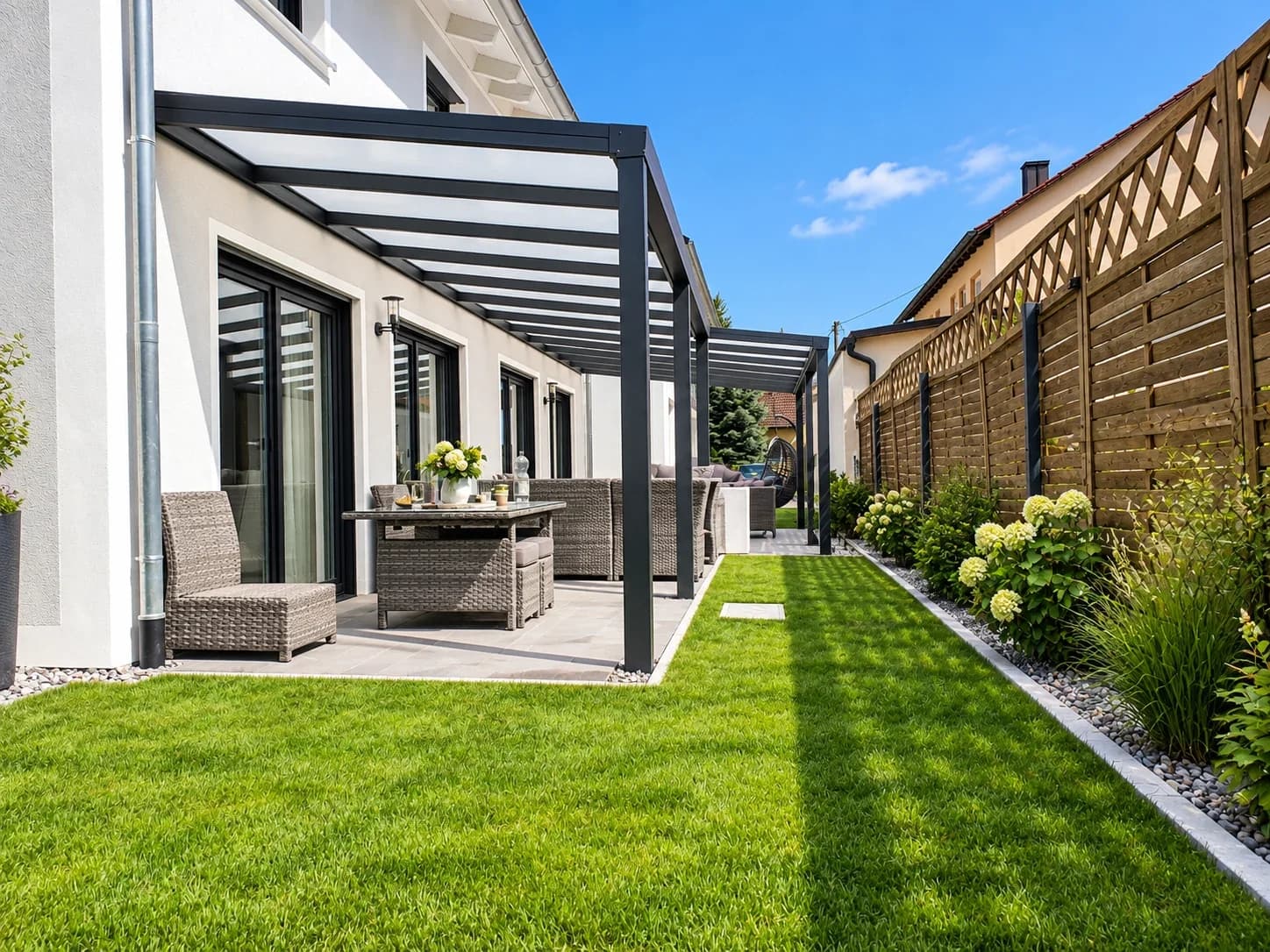 Terrassenüberdachung in Anthrazit mit lichtdurchlässiger Eindeckung entlang der Hausfassade über einer schmalen Terrasse mit Sitzgruppe