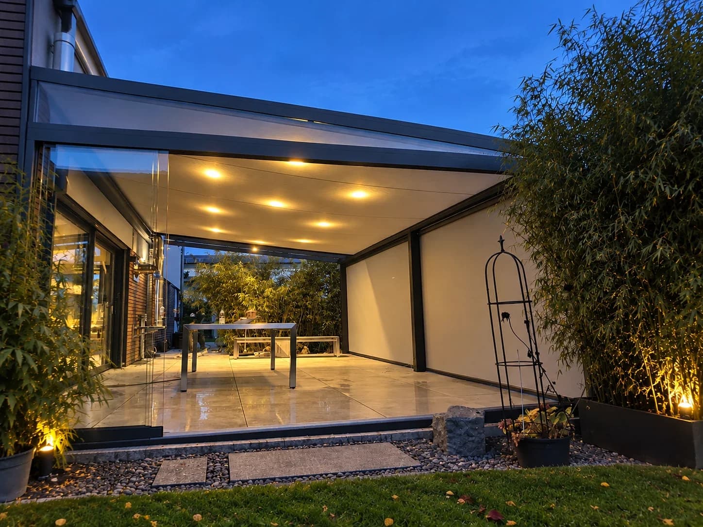 Anthrazitfarbene Terrassenüberdachung zur blauen Stunde mit warmen LED-Deckenspots